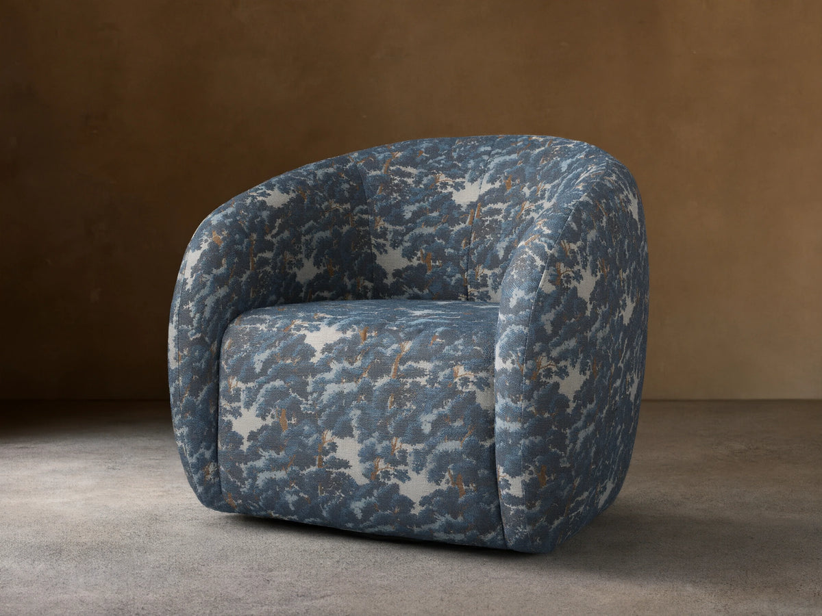 Rounded Fresno Swivel Chair upholstered in blue & brown "Oaks Pacific" tree pattern fabric, seen from front on a wooden floor.