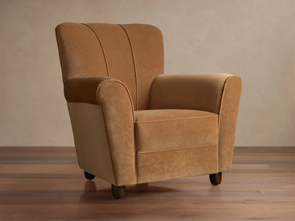 Prato Chair in Banks Camel velvet, angled. Features rolled arms, vertical channel stitching on back, on a wood floor.