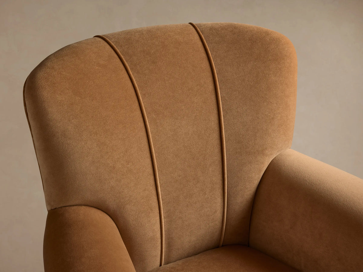 Prato Chair, front view. Upholstered in Banks Camel velvet, with rounded arms, high back, two vertical back seams. On wood floor.