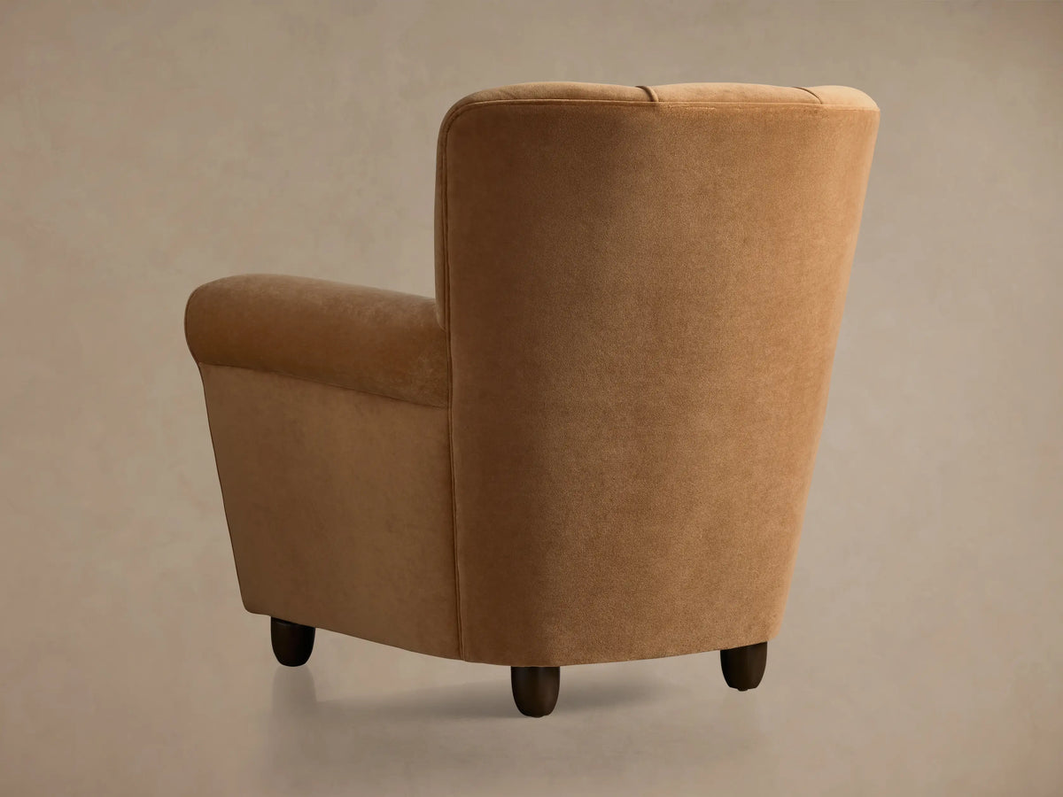 Close-up of Prato Chair's camel velvet upholstery. Curved backrest features two vertical piping details; armrest shown.
