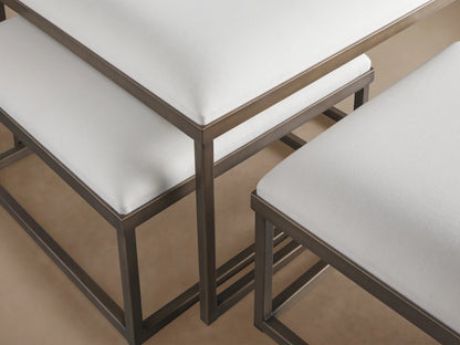 Palmer Upholstered Nesting Ottomans: Three white-cushioned ottomans with dark metal bases on a wood floor against a beige wall.