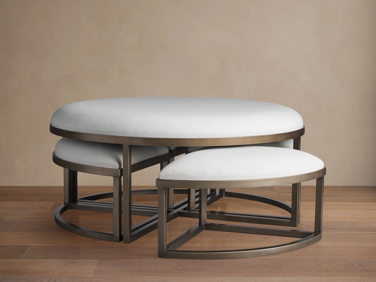 Palmer Upholstered Round Nesting Ottoman: large white top, dark metal base, smaller white ottomans nested beneath.