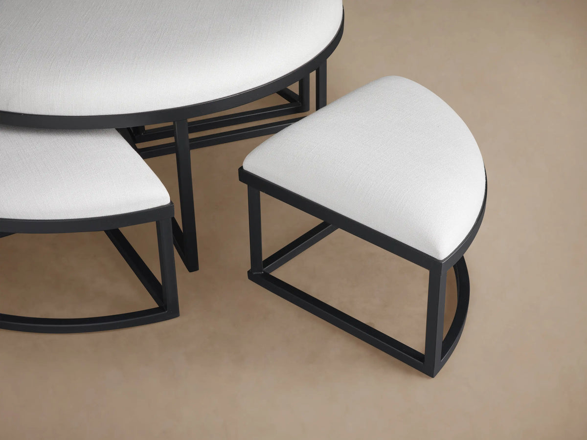 Close-up of two Palmer Round Nesting Ottomans. White upholstered tops with black metal frames, one tucked under the other.
