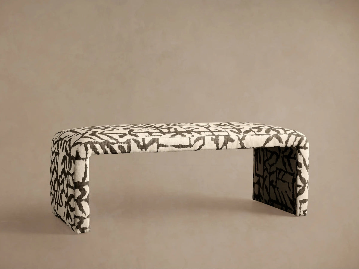Ryan Bench with a curved waterfall design, upholstered in cream fabric with a bold black abstract pattern, on a wooden floor.