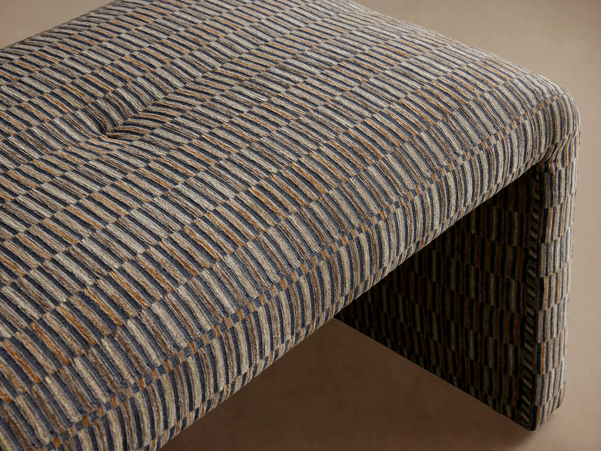 Ryan Bench upholstered in multi-toned striped fabric with brown, gray, and terracotta hues, featuring soft tufting on top.