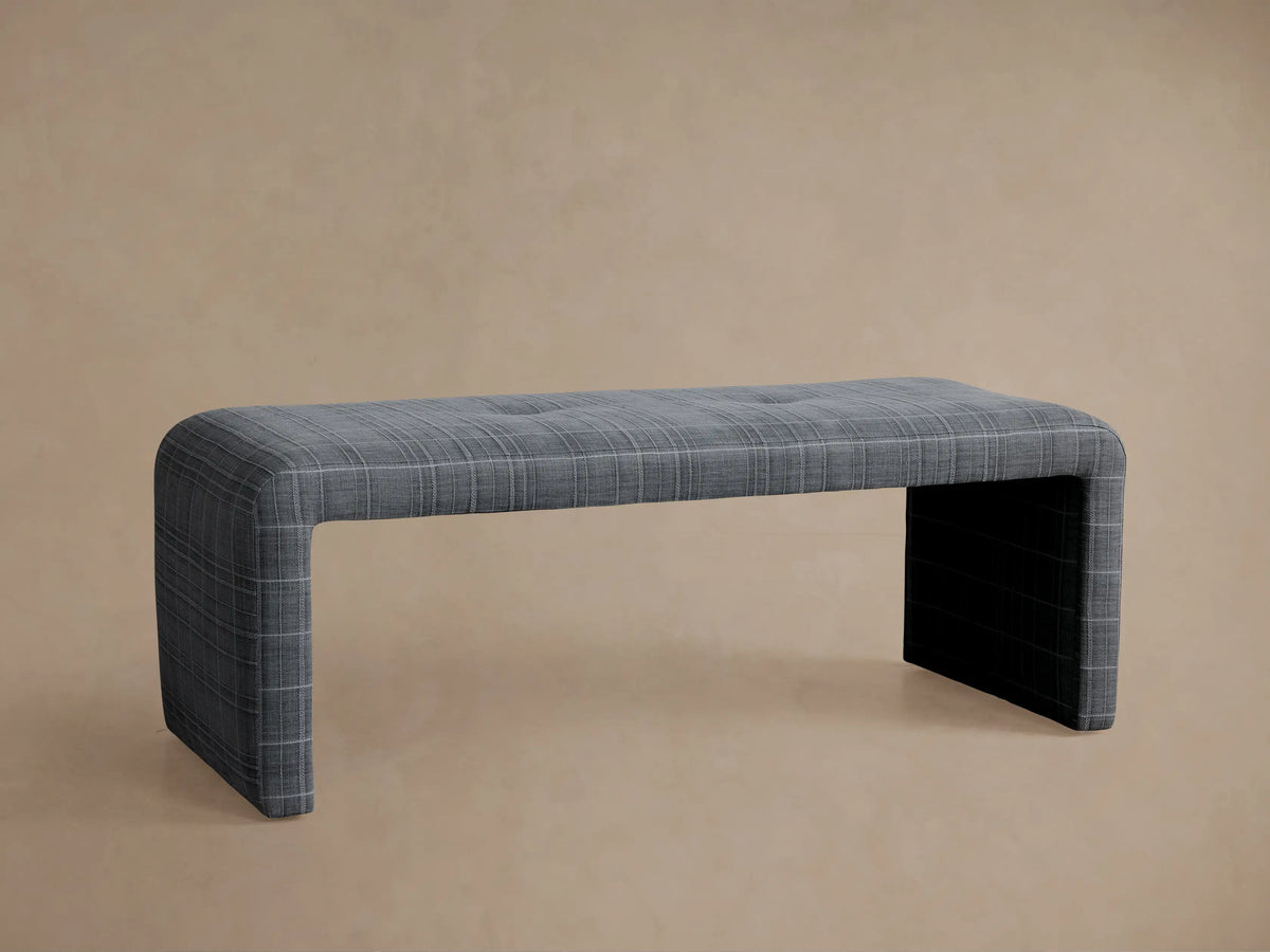 Ryan Bench, close-up angled view. Grey plaid upholstered bench with single tufting on top, fabric forms waterfall sides.