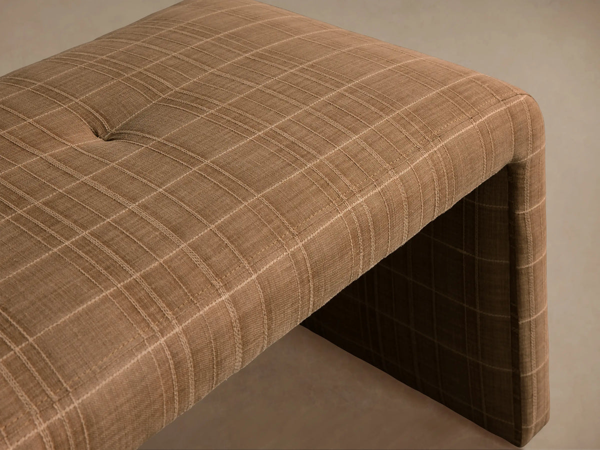Ryan Bench, tan plaid upholstered bench with curved waterfall legs and tufted seat, on a wooden floor against a neutral wall.
