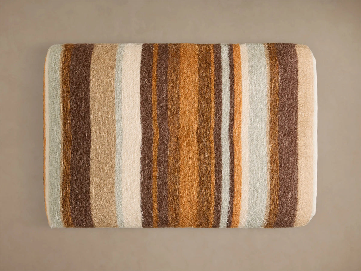 Front view of the Ryan Petite Ottoman upholstered in a striped pattern with brown, orange, cream, and pale blue.