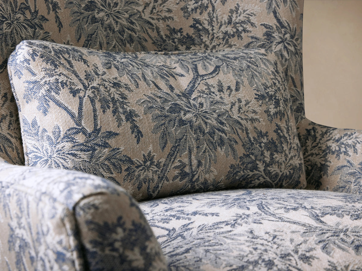 Rio Chair with high-back design in floral-patterned fabric, featuring wood legs with antique brass caster wheels, set on wooden floor.