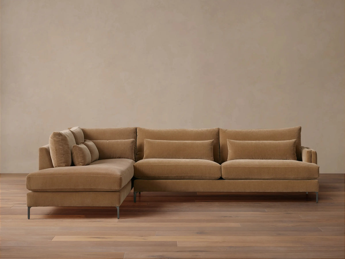 Sumner Two-Piece Bumper Sectional in light brown fabric, left chaise, three back cushions, two lumbar pillows, wooden floor, neutral wall.