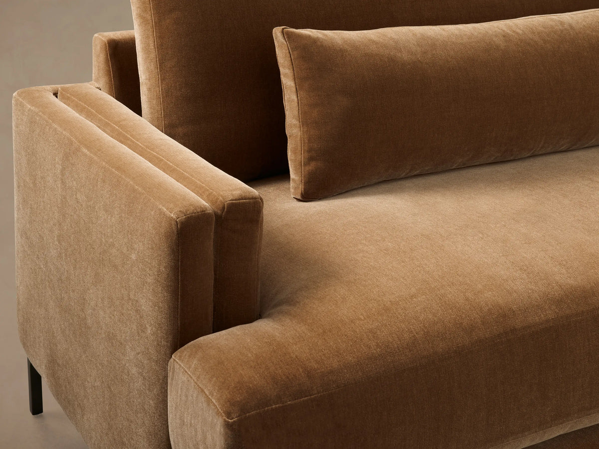 Front view of a camel brown velvet sofa with square arms, two plush back cushions, two seat cushions, and two lumbar pillows on thin dark legs.