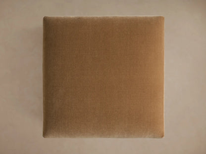 Sumner Ottoman in light brown fabric, close-up of plush cushion with square edges and metal legs, positioned against a neutral backdrop.
