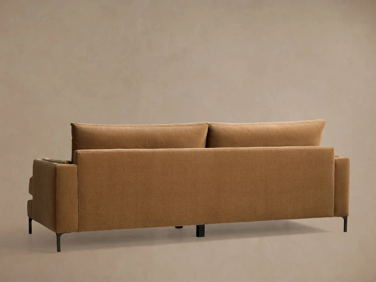 Close-up of the caramel velvet sofa, showing the square arm, seat cushion, and a back cushion with piped edges.