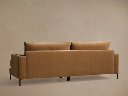 Close-up of the caramel velvet sofa, showing the square arm, seat cushion, and a back cushion with piped edges.