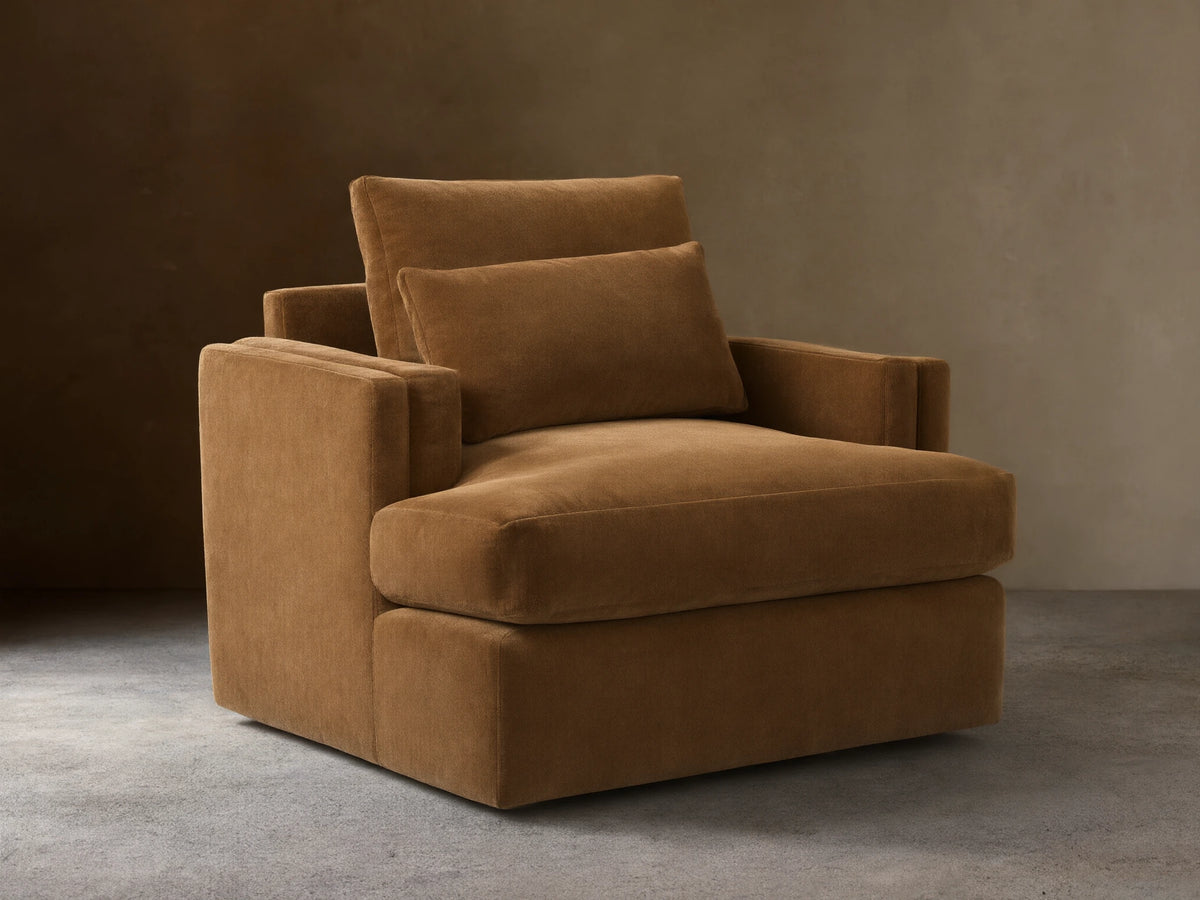 Sumner Swivel Chair in brown fabric, featuring a plush seat cushion, two padded back cushions, and solid square armrests on a hardwood floor.
