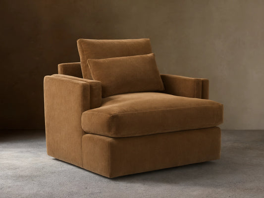 Sumner Swivel Chair in brown fabric, featuring a plush seat cushion, two padded back cushions, and solid square armrests on a hardwood floor.