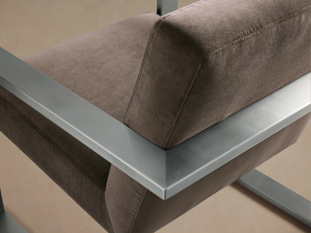 Front view of the Sabina Chair with a brown cushioned seat and backrest, supported by a geometric, metallic frame on a wooden floor.