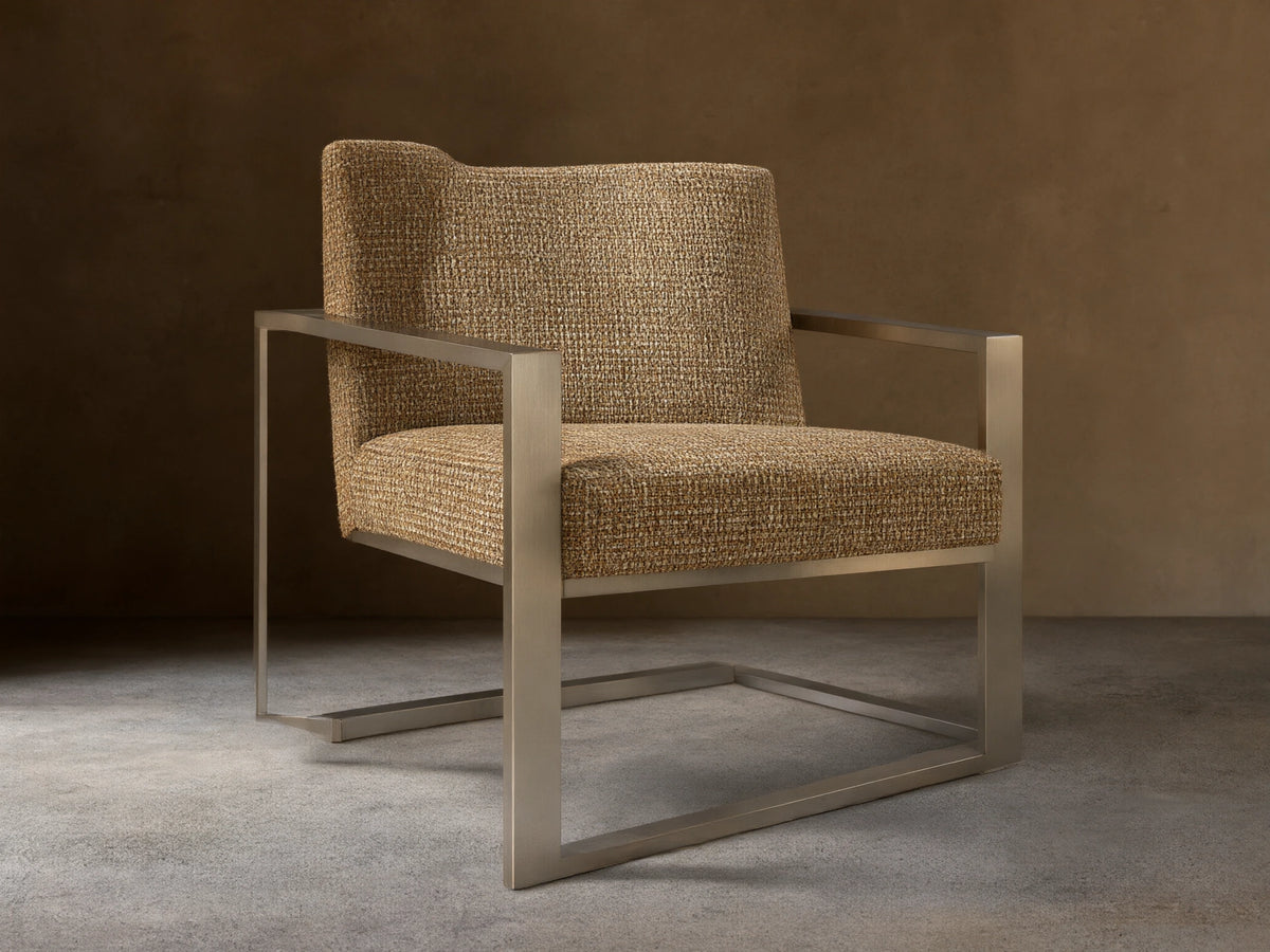 Sabina Chair with a textured beige upholstered seat and backrest, supported by sleek metallic angular legs on a wooden floor.