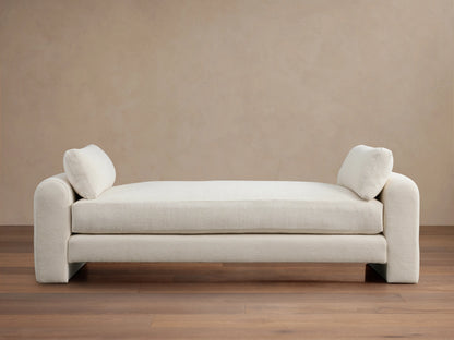 Beige Sloane Daybed on wooden floor, features plush cushions and soft fabric. Armrests and back cushions present.