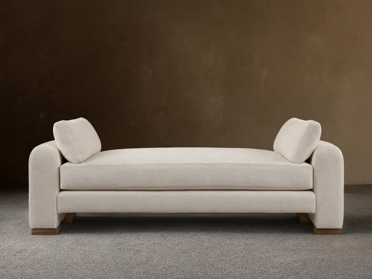 Beige Sloane Daybed on wooden floor, features plush cushions and soft fabric. Armrests and back cushions present.