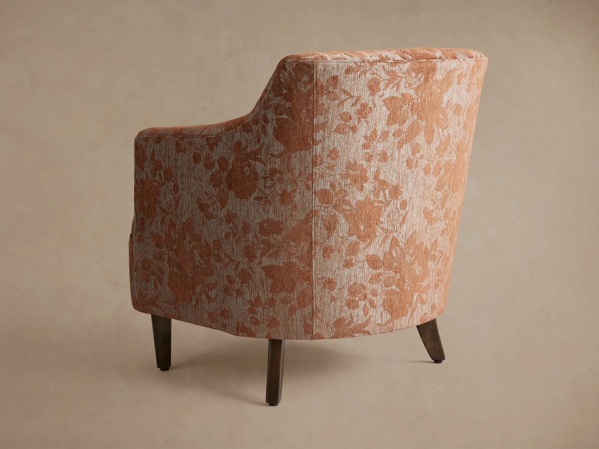 Angled close-up of Savannah Chair upholstered in rust orange floral pattern on light beige textured fabric.