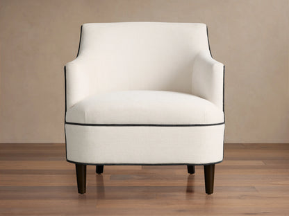 Savannah Chair: Cream upholstered armchair with black piping, dark tapered legs, angled on a wood floor.