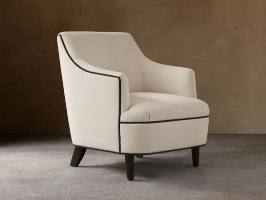 Savannah Chair: Cream upholstered armchair with black piping, dark tapered legs, angled on a wood floor.