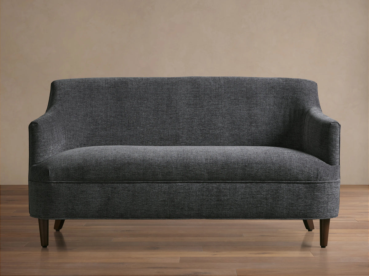 Dark gray textured Savannah Settee with curved back and arms, on dark tapered wood legs, centered against a neutral wall.