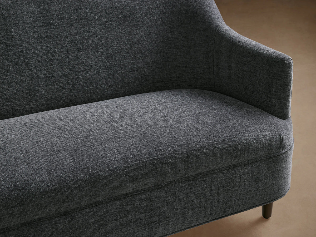 Savannah Settee, upholstered in dark gray textured fabric, showing a curved armrest, cushioned seat, and dark wooden legs.