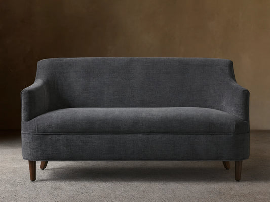 Dark gray textured Savannah Settee with curved back and arms, on dark tapered wood legs, centered against a neutral wall.