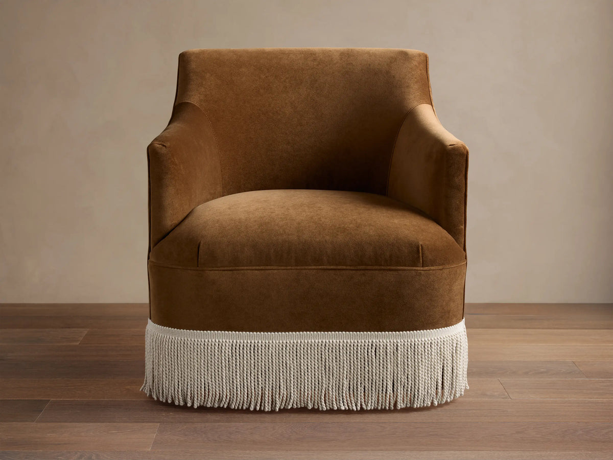 Rich brown velvet Savannah Swivel Chair with white fringe detail, angled on a dark wood floor against a light wall.