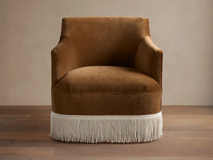 Rich brown velvet Savannah Swivel Chair with white fringe detail, angled on a dark wood floor against a light wall.