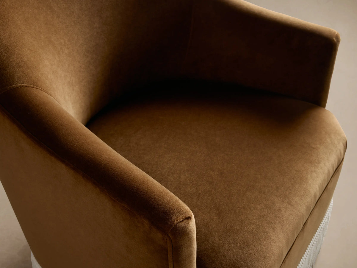 Warm brown Savannah chair with curved back and cream fringe skirt, angled slightly right on a wood floor.