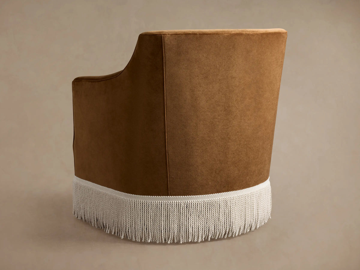 Close-up of a Savannah Swivel Chair, upholstered in rich caramel velvet, showing the armrest, seat, and silver fringe.