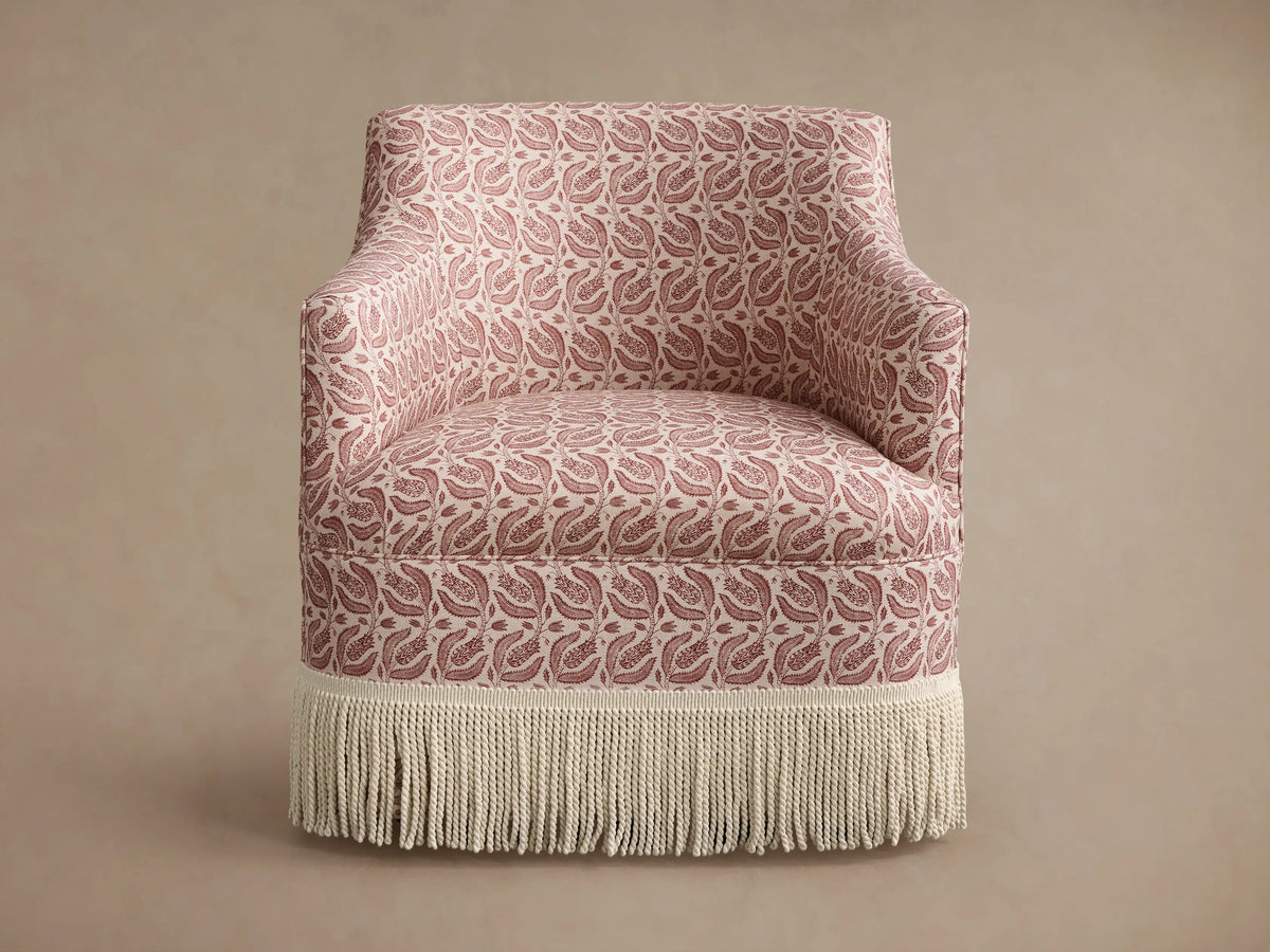 Savannah Swivel Chair with Fringe, pink & cream botanical pattern upholstery, cream fringe base, shown at an angle.