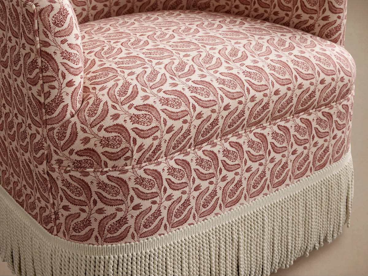 Savannah Swivel Chair: Cream fabric with dense reddish-brown leaf pattern, long cream knotted fringe base, front view.