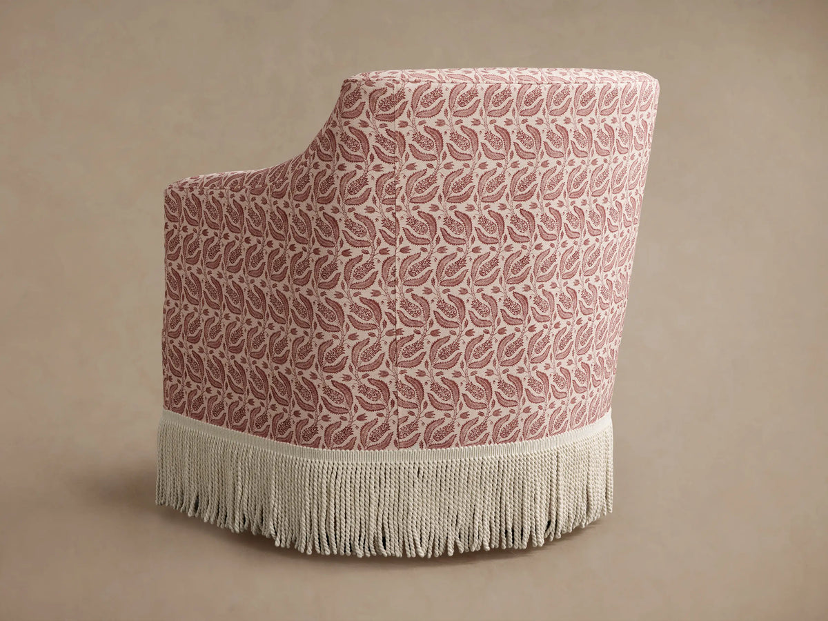 Close-up of Savannah Swivel Chair. Beige fabric with red botanical pattern and cream fringe detail at the bottom.