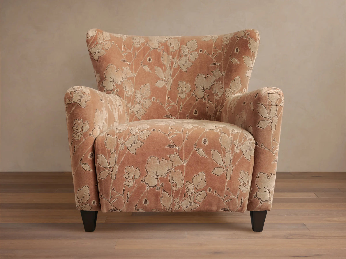 Front view of the muted peach Sasha Chair with cream floral pattern, rolled arms, and dark wood legs.