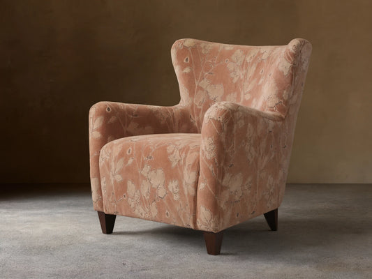 Front view of the muted peach Sasha Chair with cream floral pattern, rolled arms, and dark wood legs.