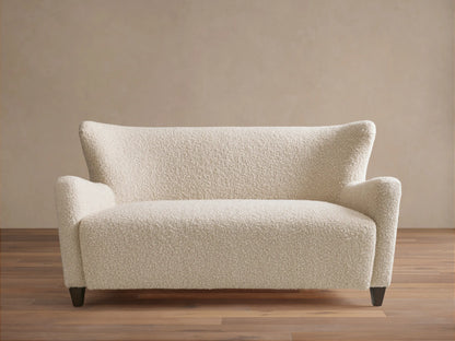 Sasha Settee in cream fabric featuring a textured, boucle finish, angled arms, and tapered dark wooden legs on a wooden floor.
