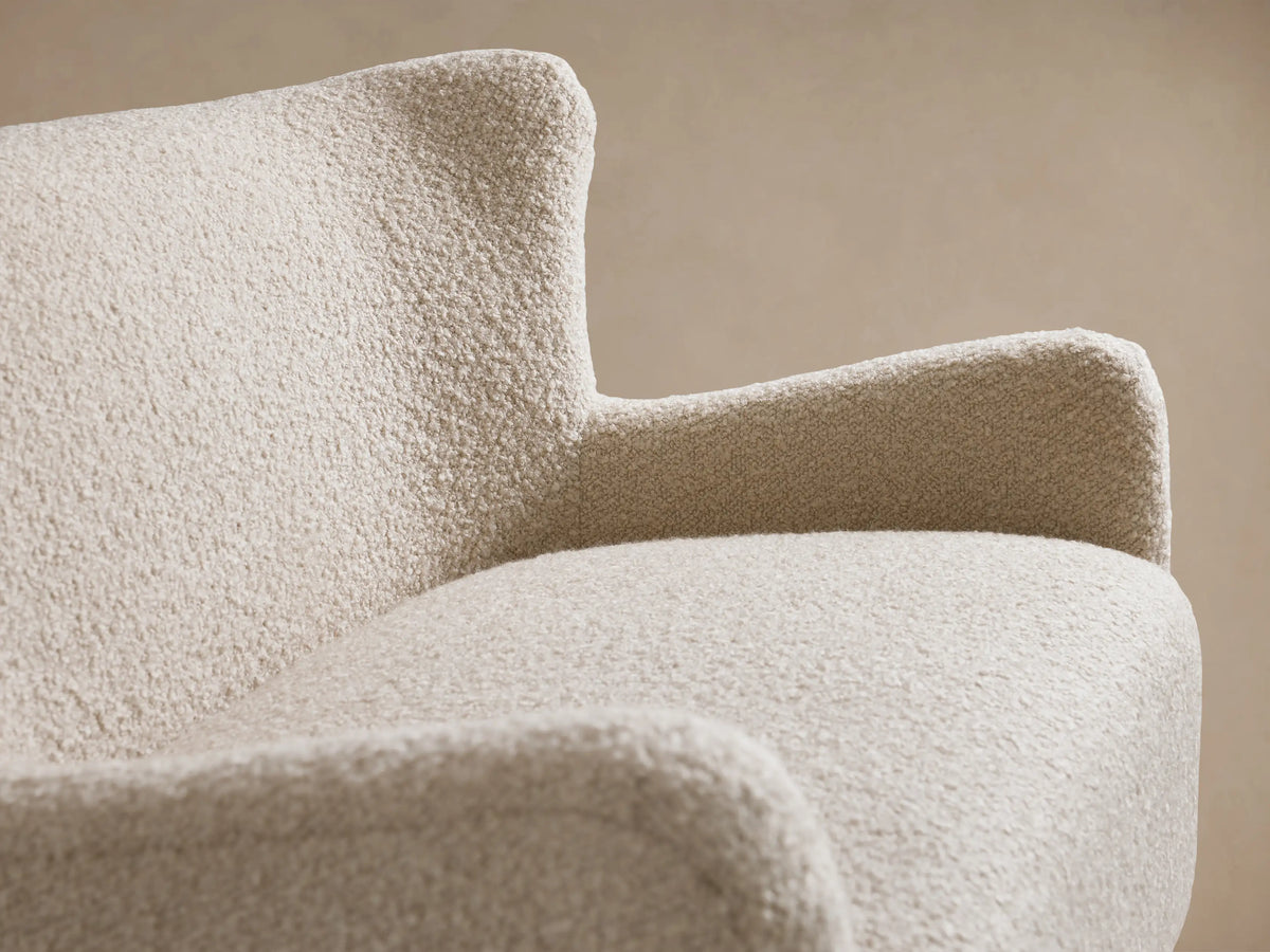Cream-colored Sasha Settee with curved arms and backrest, upholstered in textured fabric. Black legs, set on wooden floor.