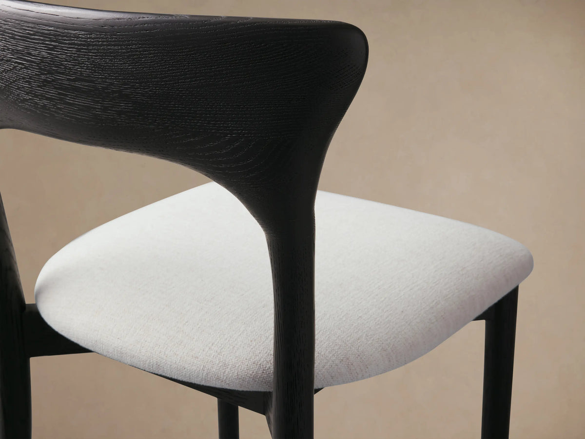 Sinclair Dining Chair, black oak frame with a curved backrest and light upholstered seat, centered on a wood floor.
