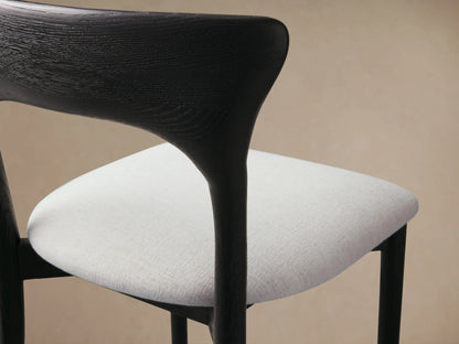 Sinclair Dining Chair, black oak frame with a curved backrest and light upholstered seat, centered on a wood floor.