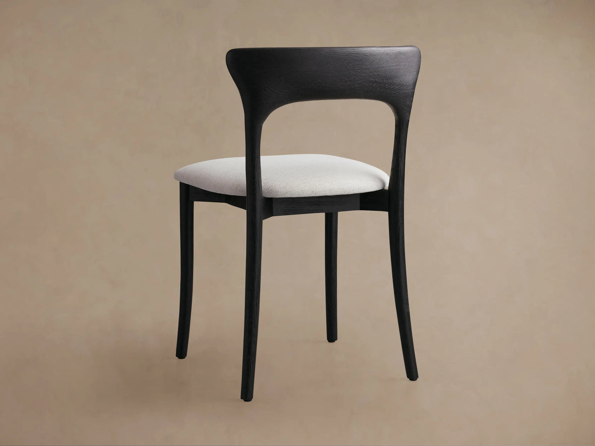 Close-up of Sinclair Dining Chair, dark curved oak backrest with visible grain, light textured fabric seat, angled view.