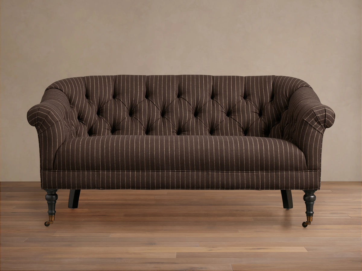 Tangier Settee in brown with white pinstripes, features curved arms and tufted backrest. Supported by wooden legs with casters.