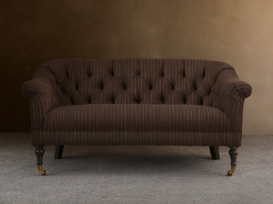 Tangier Settee in brown with white pinstripes, features curved arms and tufted backrest. Supported by wooden legs with casters.