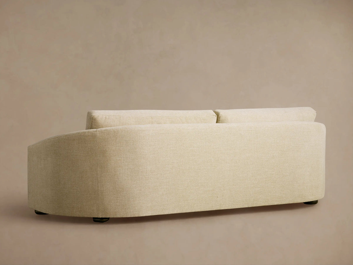 Close-up of the Avon Sofa, showing the light beige textured fabric of the back cushion and curved armrest against a beige wall.