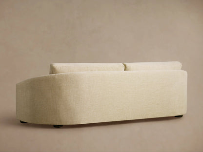 Close-up of the Avon Sofa, showing the light beige textured fabric of the back cushion and curved armrest against a beige wall.