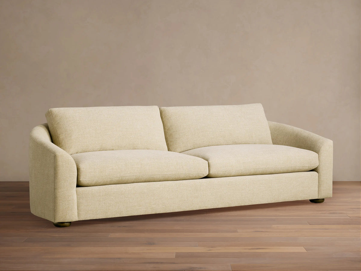 Light beige Avon Sofa with plump cushions and curved arms, accented by two pillows, in a sunlit living room.