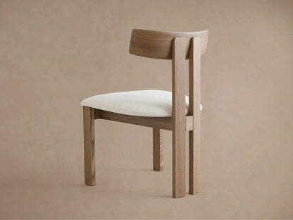 Rodin Wood Back Dining Chair. Light ash wood frame, curved backrest, and white textured fabric seat, angled view against beige wall.